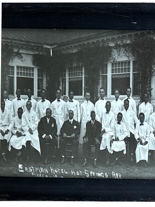 "Eastman Hotel Hot Springs Ark. March 1919," a photo of approximately 60 African American men in two rows, one sitting in front and the other standing behind. 67 are wearing buttoned up white coats with bowtie or tie; the other three, probably the highest ranking, are wearing dark suits and seated in the center of the front row.
